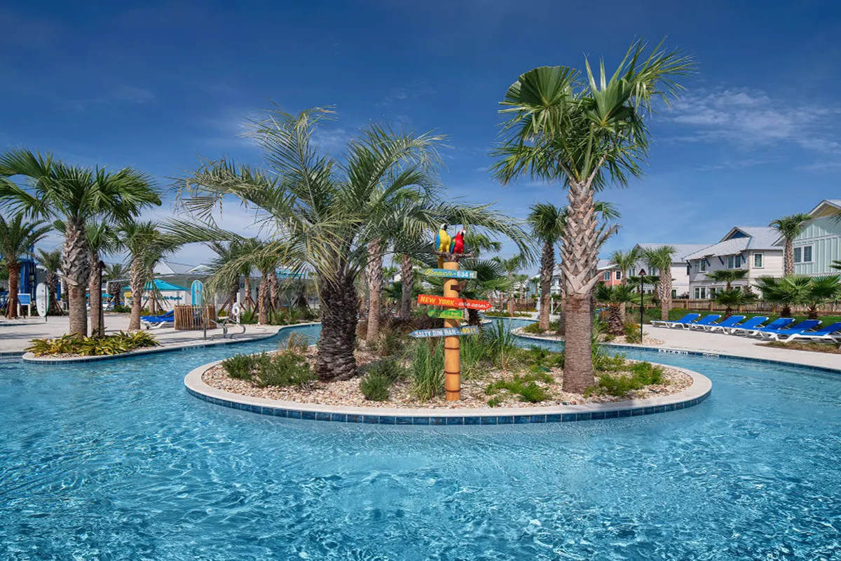 A vibrant scene of a lazy river winding through tropical landscaping, dotted with palm trees and surrounded by modern resort buildings and blue lounge chairs. A colorful signpost with parrots adds a playful, vacation-like touch, while guests float leisurely in the clear water and relax poolside.