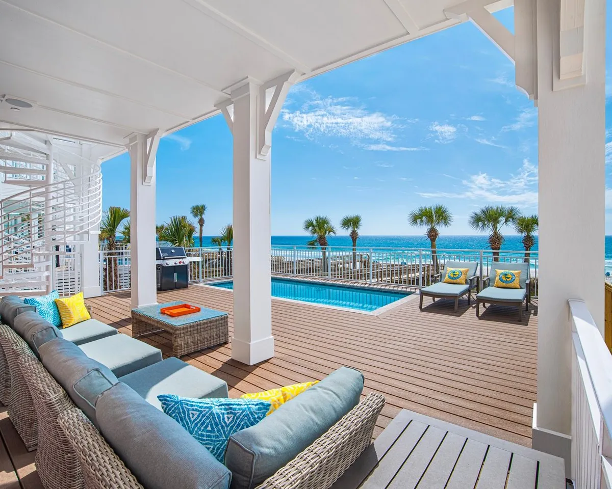 A bright, inviting beachfront patio with a private heated pool, comfortable outdoor seating with colorful cushions, and a spiral staircase leading to upper floors. The patio offers unobstructed ocean views, blending relaxation and social opportunities with the beauty of the Gulf.