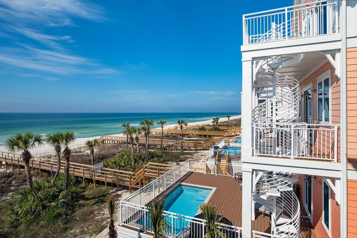 This image features a private heated swimming pool adjacent to a villa, a white spiral staircase leading up to a balcony, and a wooden dune walkover providing direct access to a pristine sandy beach and turquoise Gulf waters. The scene conveys a sense of privacy, luxury, and seamless transition from the villa to both the pool and the beach.